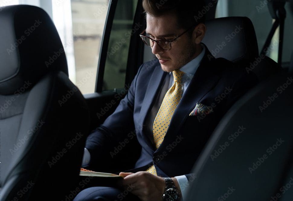 Book a St. Louis Blues Game Limo | Gateway Black Car Service 4 A professional businessman in a dark suit, gold tie, and glasses reading a document in the backseat of a luxury black car, representing Gateway Limousine's executive car service in St. Louis and Chesterfield.